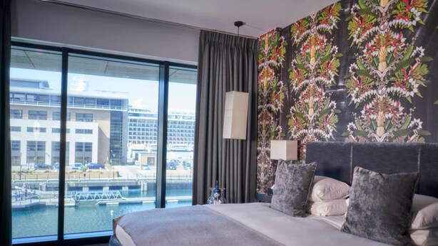 A hotel room with a large bed, a view of a cityscape through floor-to-ceiling windows, and a floral-patterned wall. - Malmaison Liverpool (Liverpool)