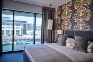 A hotel room with a large bed, a view of a cityscape through floor-to-ceiling windows, and a floral-patterned wall. - Malmaison Liverpool (Liverpool)