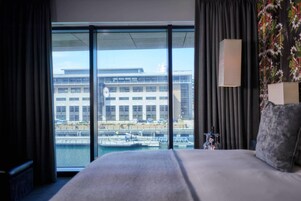Habitación de hotel con una cama grande, vistas a un edificio al otro lado del agua y una lámpara en la pared.