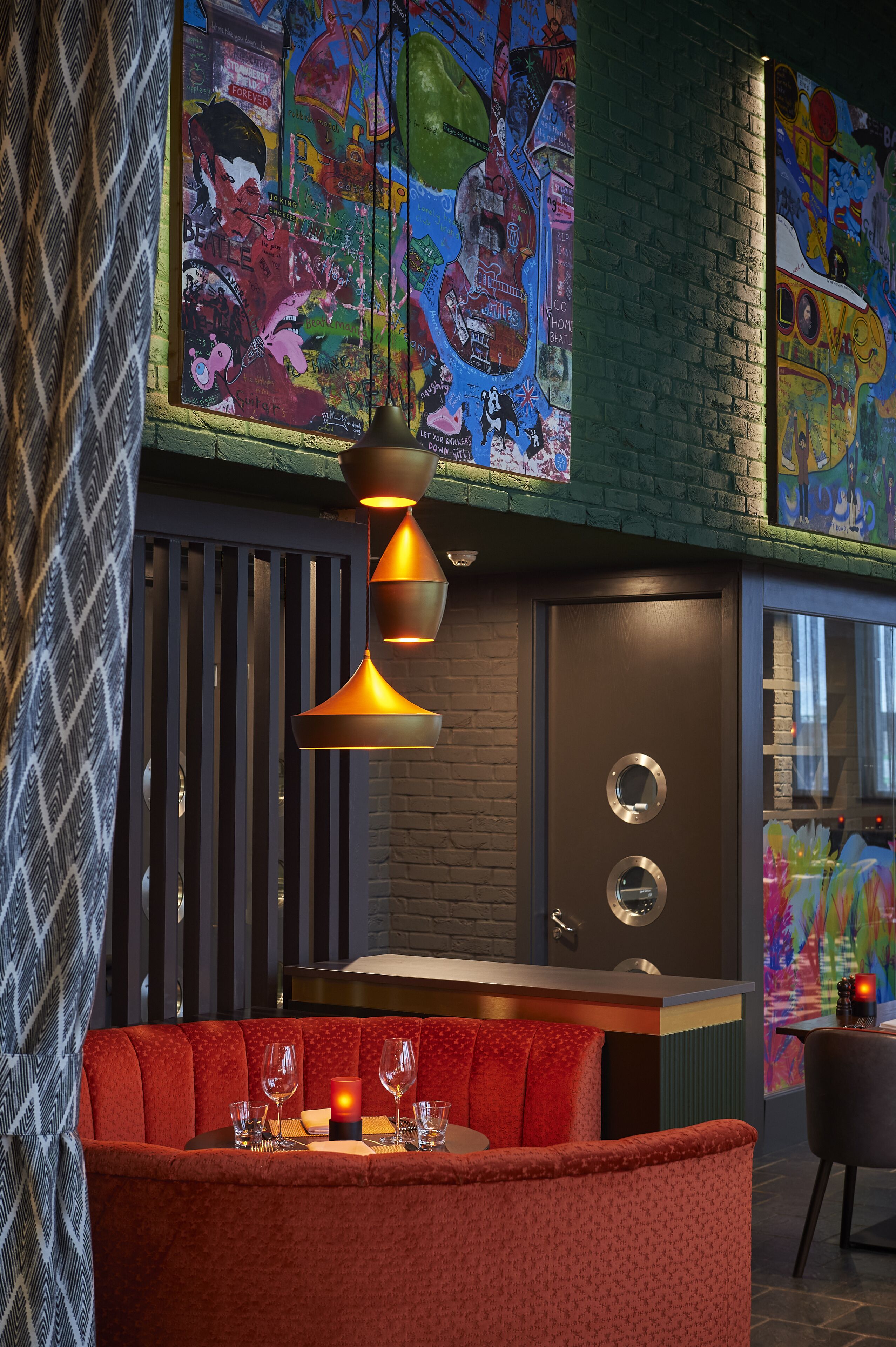 Un restaurante con zona de asientos en una cabina roja, una barra y arte callejero colorido en las paredes.
