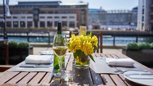 A table set with a wine bottle, glasses, a vase with yellow flowers, and a placemat with a number sign. - Malmaison Liverpool (Liverpool)