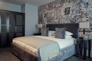 A neatly made bed with a grey headboard, a dark wardrobe, and a wall with a city map design.