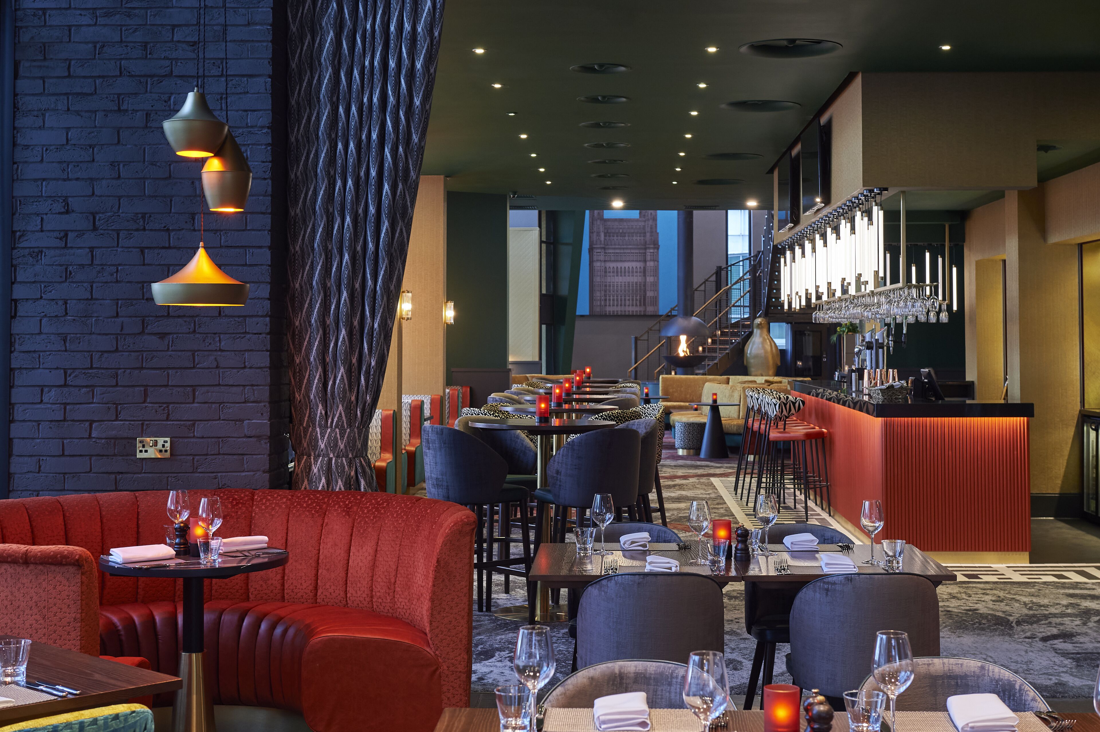 En restaurant med røde polstrede bænke, et barområde med rødt skranke og en trappe, der fører op til et højere niveau.