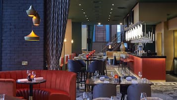 Un restaurante con cabinas tapizadas de rojo, una zona de bar con mostrador rojo y una escalera que sube a un nivel superior.