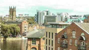 A riverside view of a city with historic buildings, a prominent clock tower, and modern high-rises in the background.
