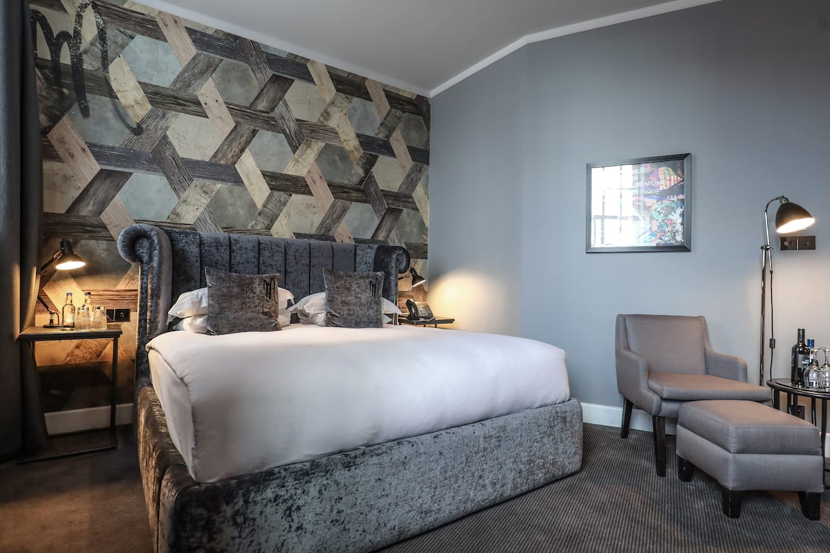 A modern hotel room with a large bed, a seating area, and a wall with a geometric pattern.