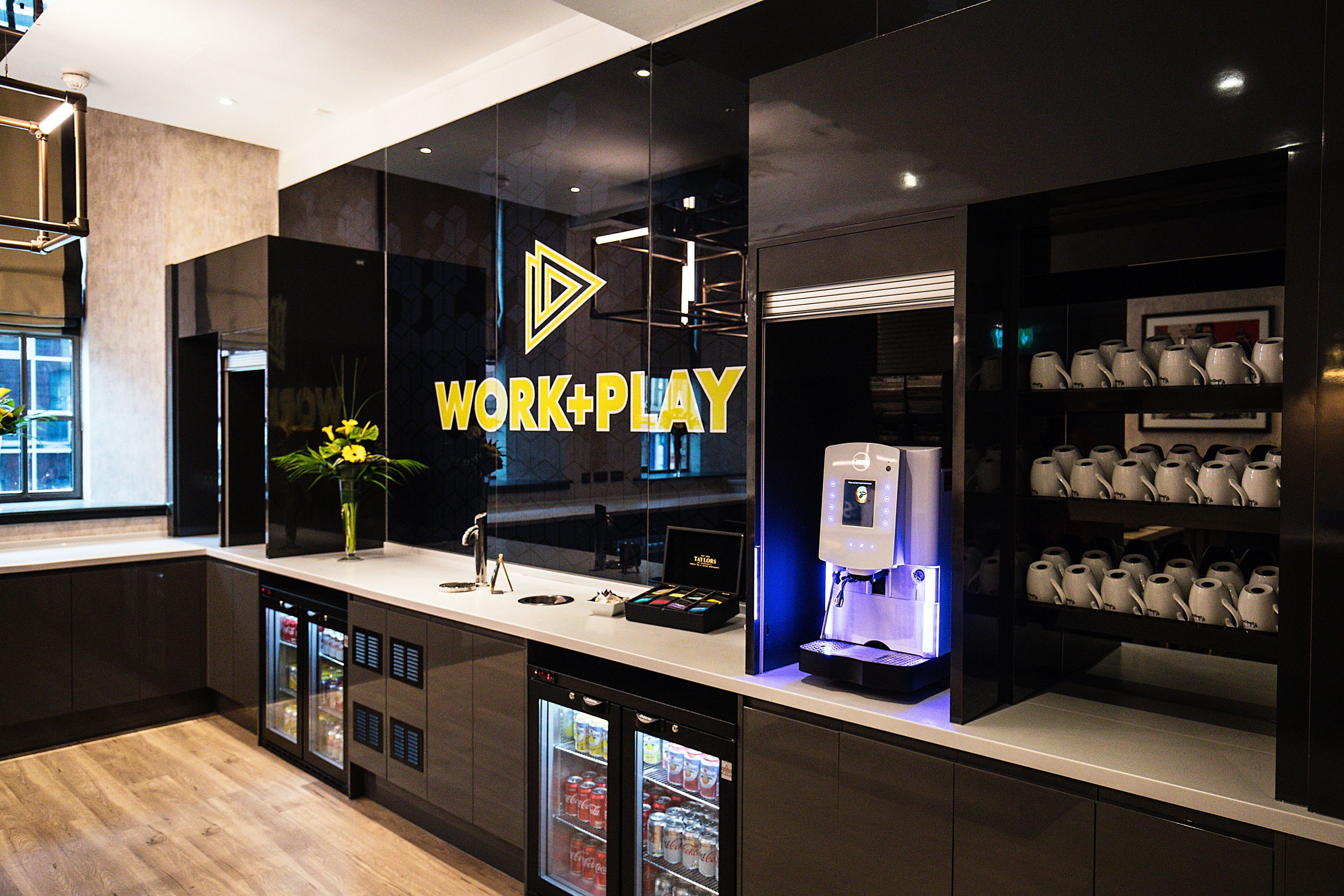 A modern kitchen with a "WORK+PLAY" sign, a coffee machine, and built-in refrigerators.