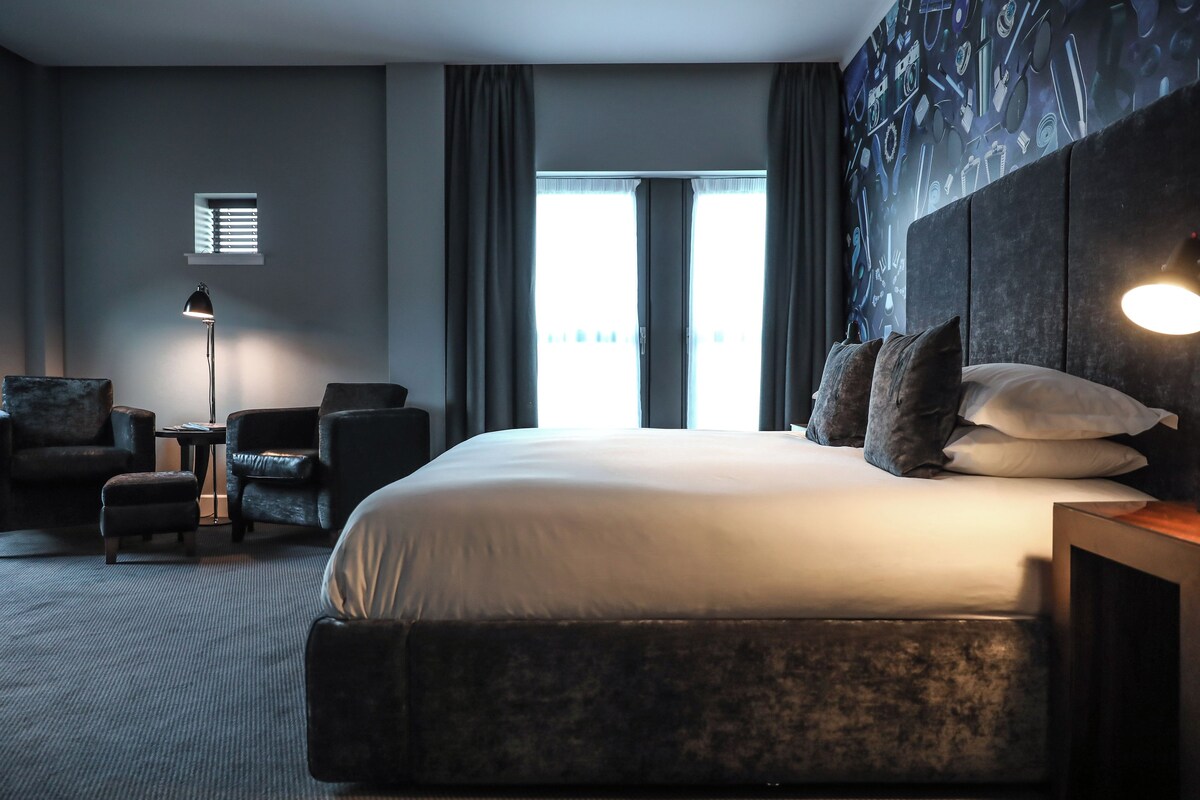 A hotel room with a large bed, two armchairs, a small table, and a floor lamp.
