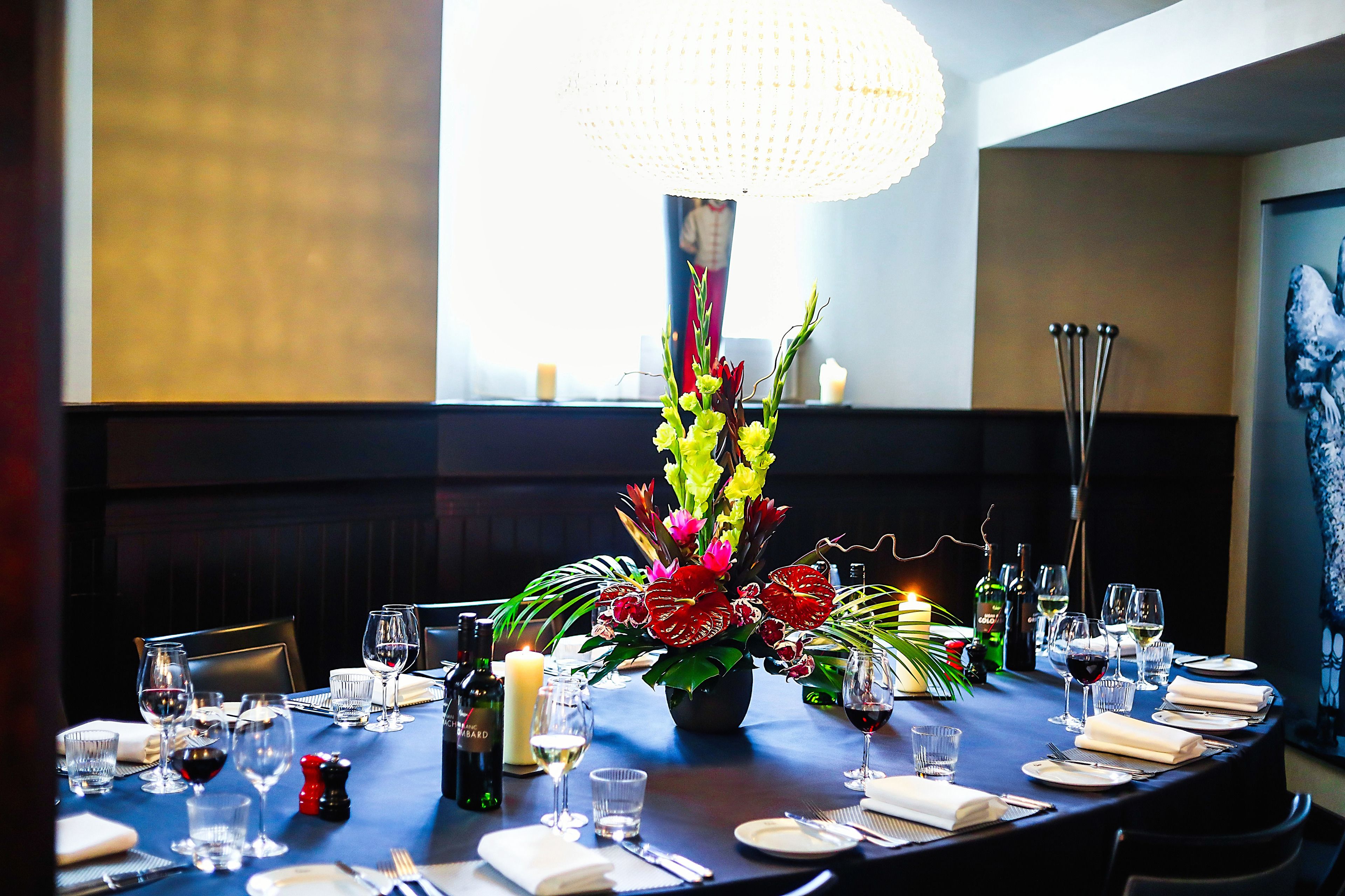 A dining table set for a meal with a centerpiece of flowers, candles, and wine glasses.