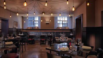 A restaurant with multiple tables, chairs, and hanging light bulbs.