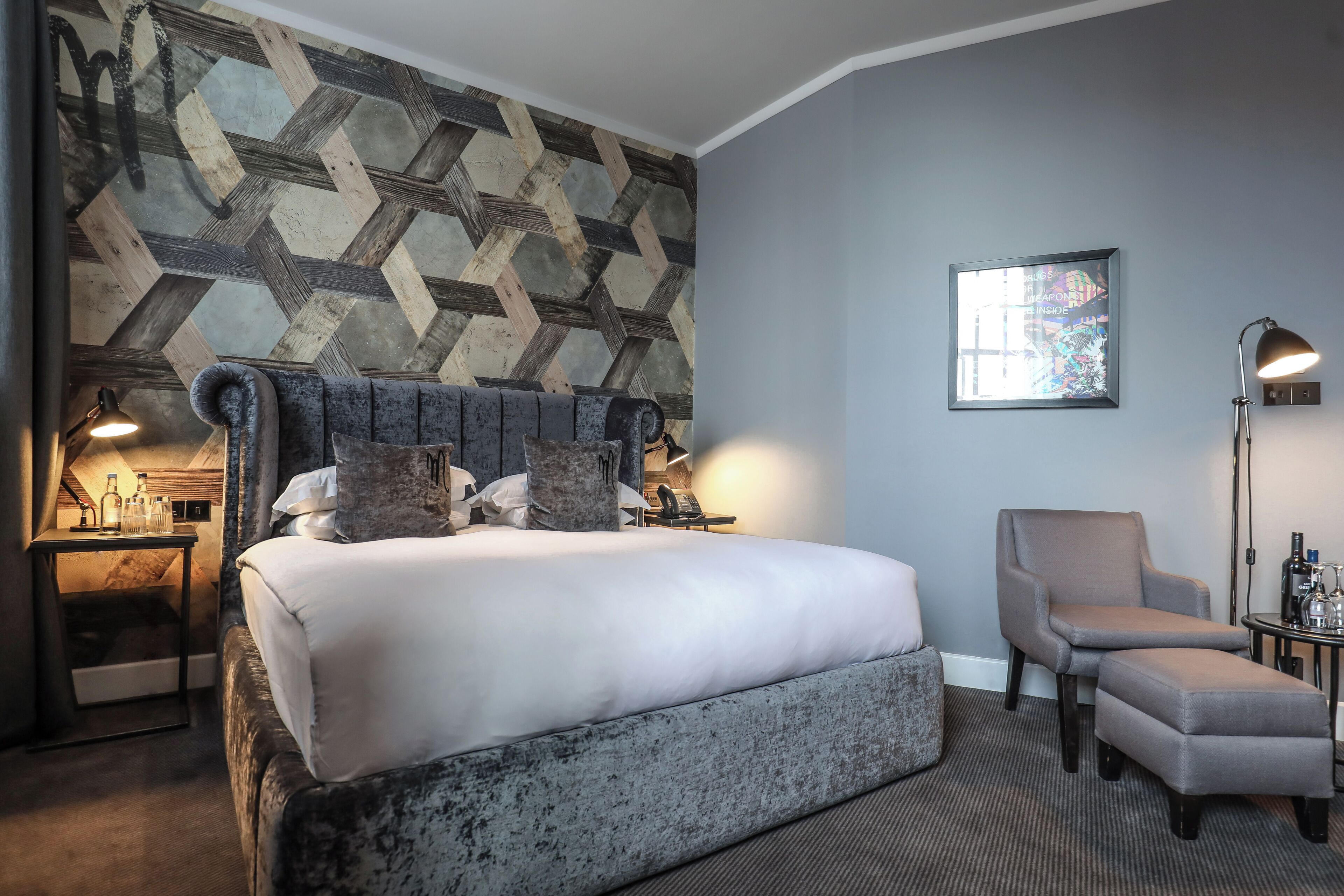 Una habitación de hotel con una cama grande, una silla, un escritorio y una pared con un diseño geométrico.