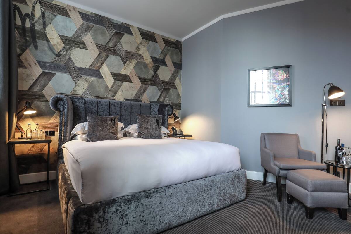 A hotel room with a large bed, a chair, a desk, and a wall with a geometric pattern.