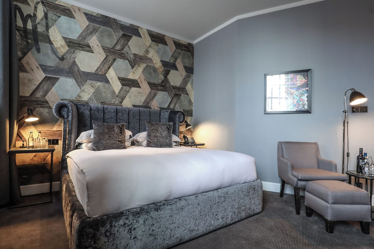 A hotel room with a large bed, a chair, a desk, and a wall with a geometric pattern.