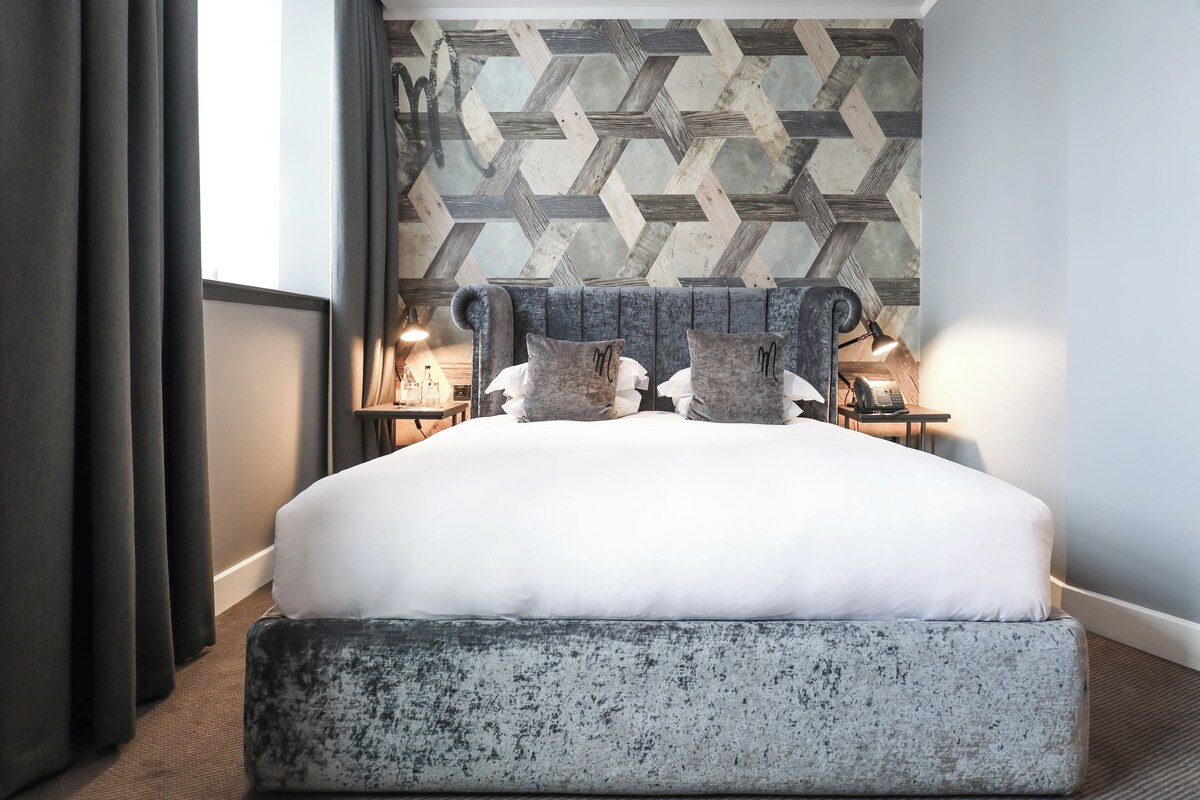 A bed with a headboard, pillows, and a bedside table with lamps.