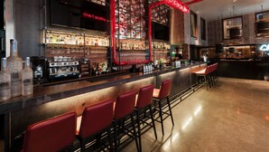 Zona de bar con diseño moderno, que incluye una barra con taburetes, una variedad de botellas y un letrero de neón.