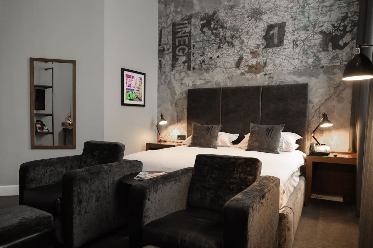 A hotel room with a large bed, two bedside tables with lamps, a map on the wall, and four armchairs.