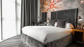 A modern hotel room with a large bed, a desk, and a view of the city.