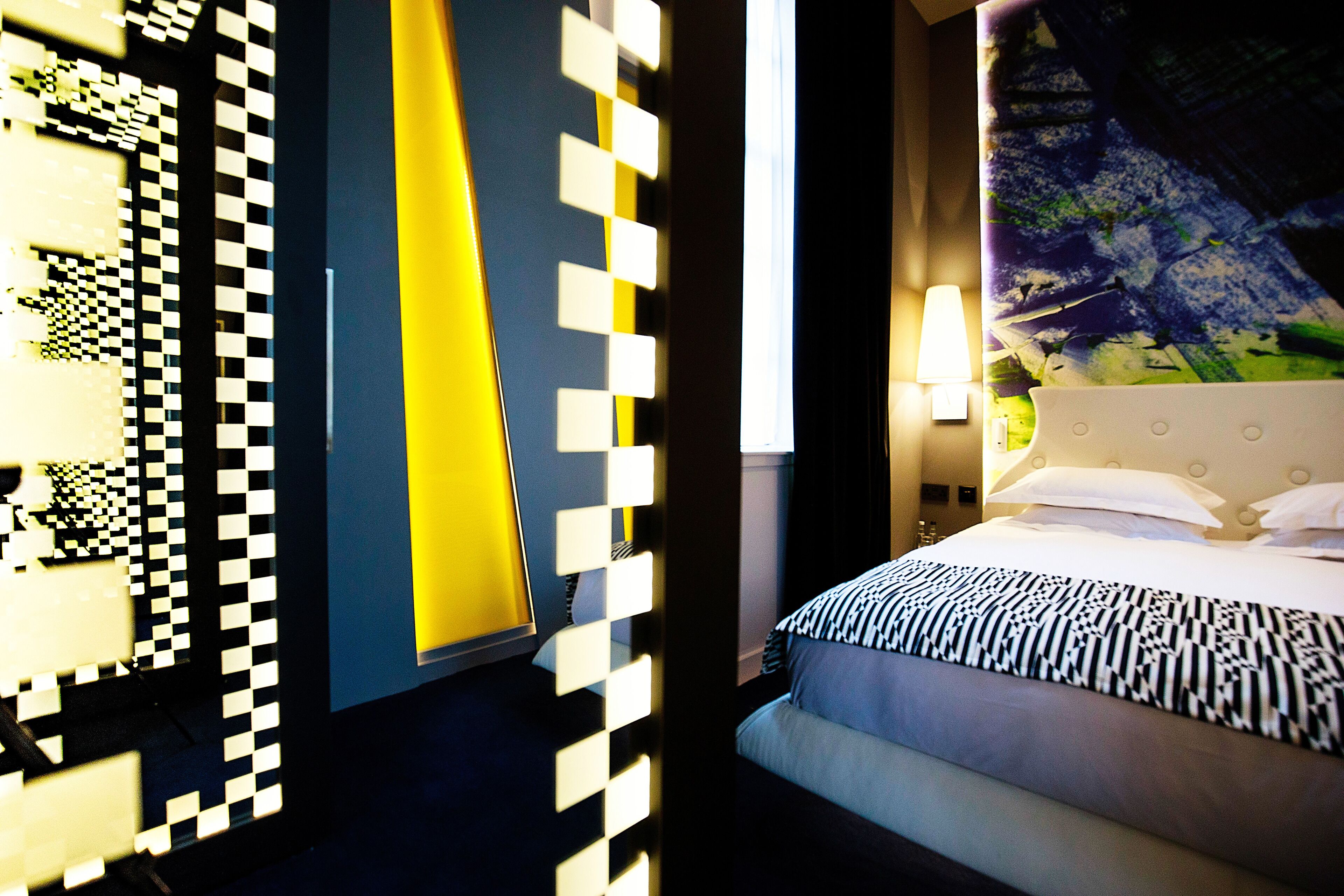 Une chambre d’hôtel avec un lit, une tête de lit, un mur orné d’un motif et une lampe.
