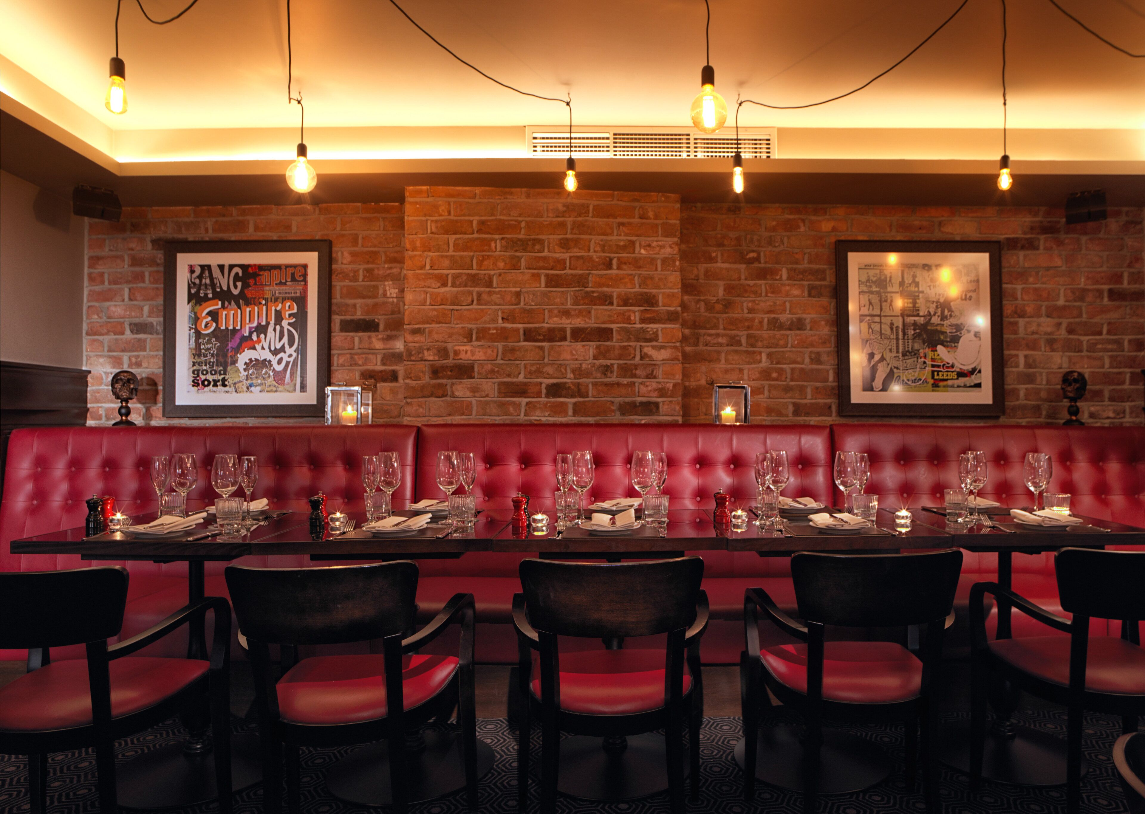A restaurant with a brick wall, red cushioned booths, and a long dining table set with chairs.