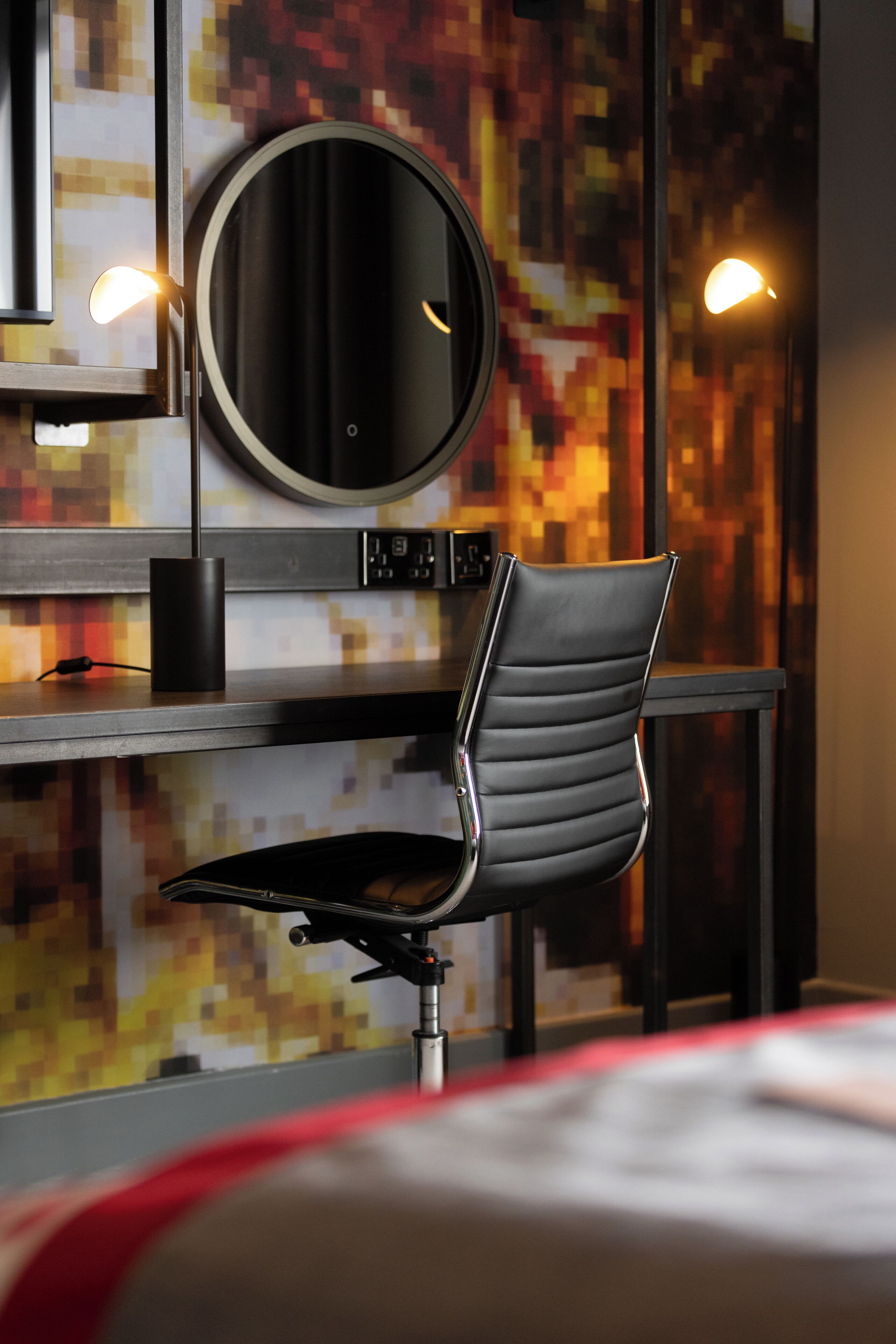 Una habitación moderna con un espejo redondo, una silla negra y una pared con un diseño pixelado.