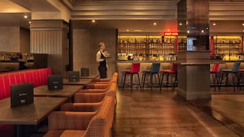 A bar area with a bartender, red and blue bar stools, and a well-stocked bar counter.