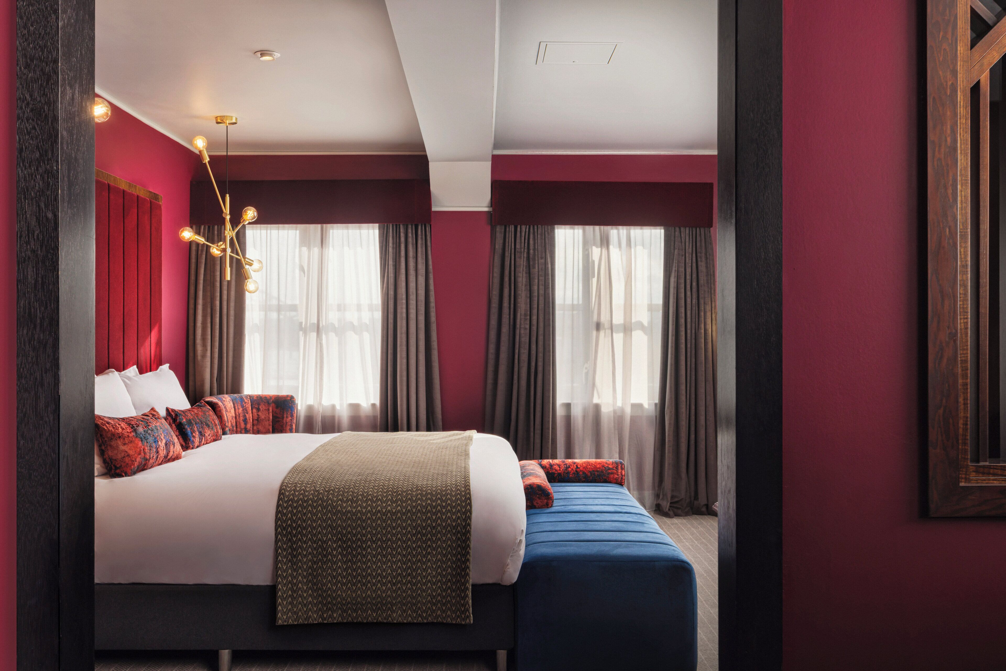 A modern hotel room with a large bed, a bedside table, a desk, and a window with curtains.