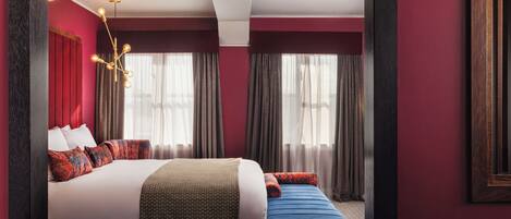 A modern hotel room with a large bed, a bedside table, a desk, and a window with curtains.
