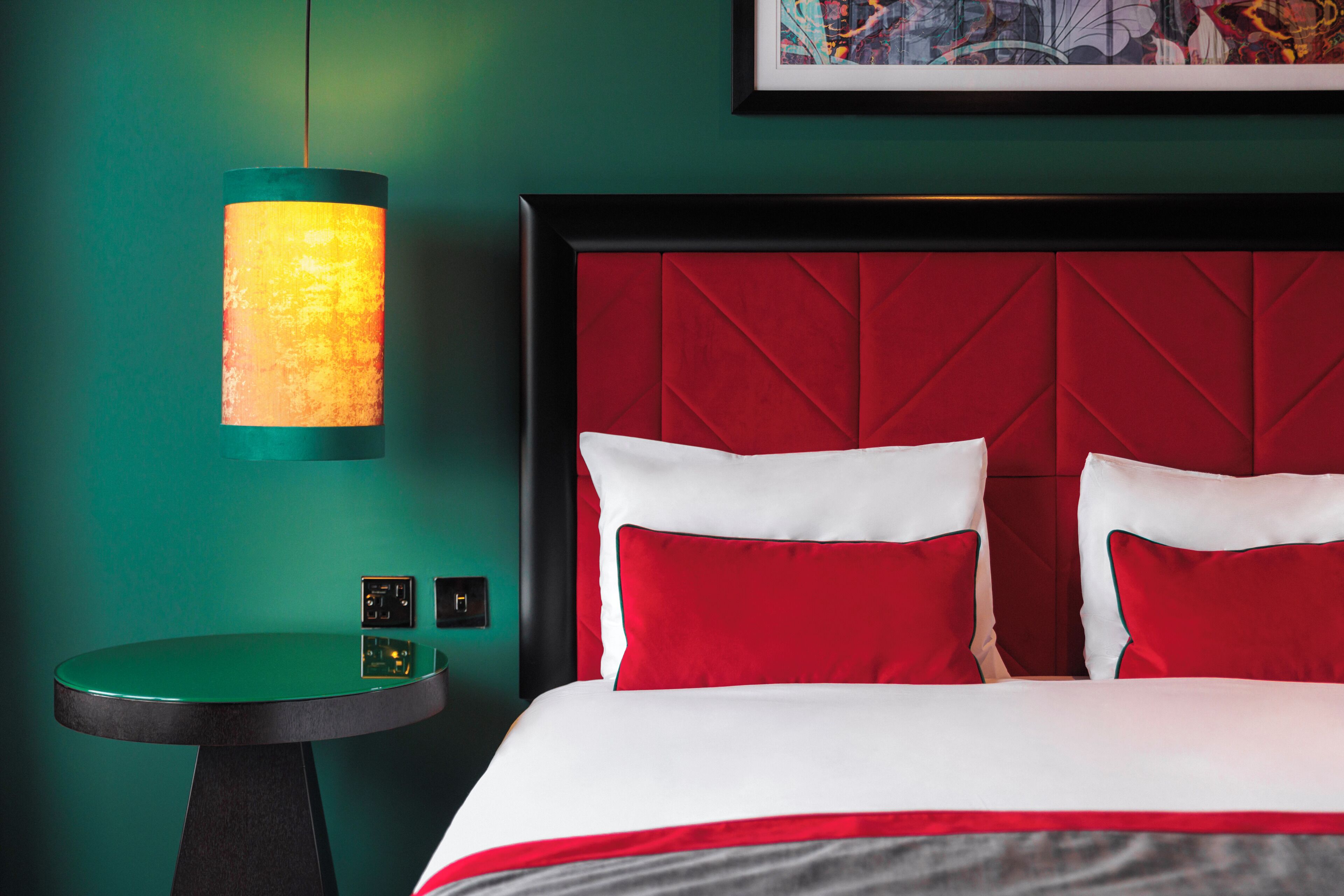 Una habitación de hotel con cabecera roja, una mesa redonda y una lámpara de pared.