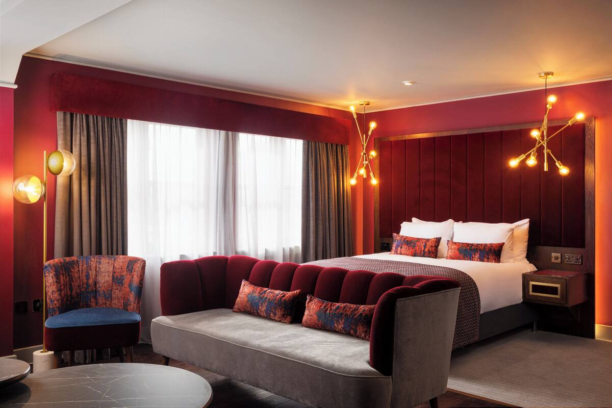 A hotel room with a large bed, a sofa, a chair, and a small table.