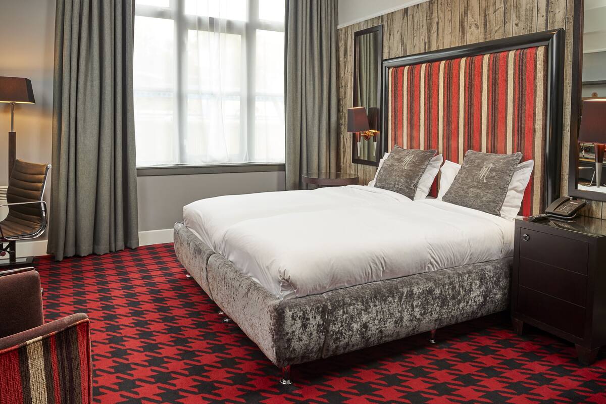 A hotel room with a large bed, a chair, a nightstand, a lamp, and a window with curtains.