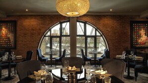 A restaurant with a brick wall, large arched windows, and a chandelier. Tables are set with wine glasses and plates. - Malmaison Newcastle (Newcastle-upon-Tyne)