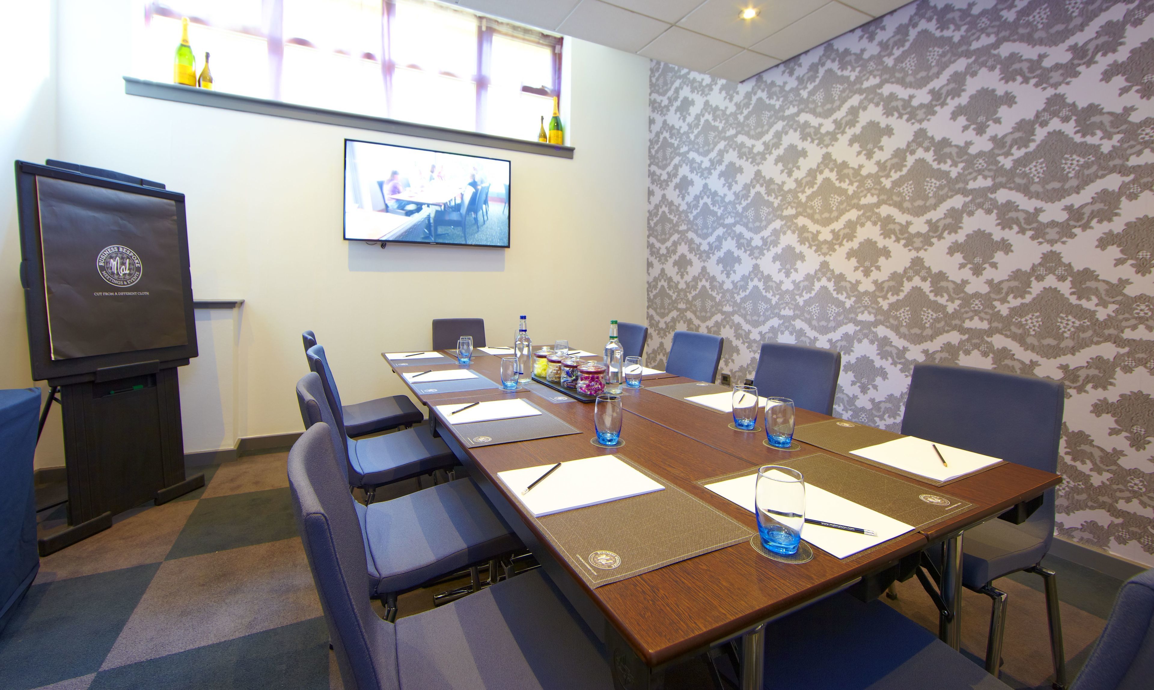 A conference room with a long table, chairs, a projector screen, and a patterned wall.
