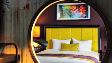 A hotel room with a yellow headboard, white bedding, and a colorful abstract painting above the bed.