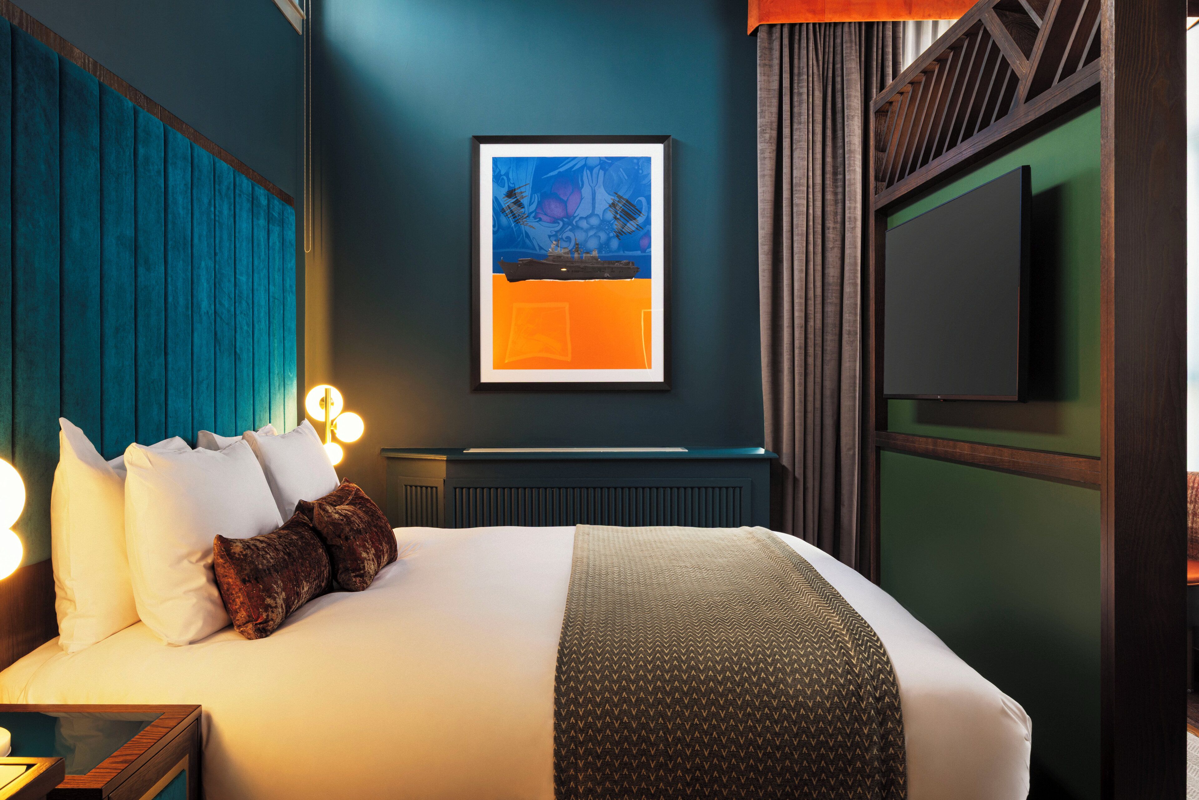 Una habitación de hotel con una cama, una obra de arte enmarcada, un televisor y una ventana con cortinas.