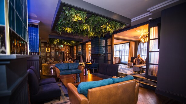 A modern lounge with a high ceiling, green plants, and a mix of seating areas including sofas and armchairs. - Malmaison Newcastle (Newcastle-upon-Tyne)