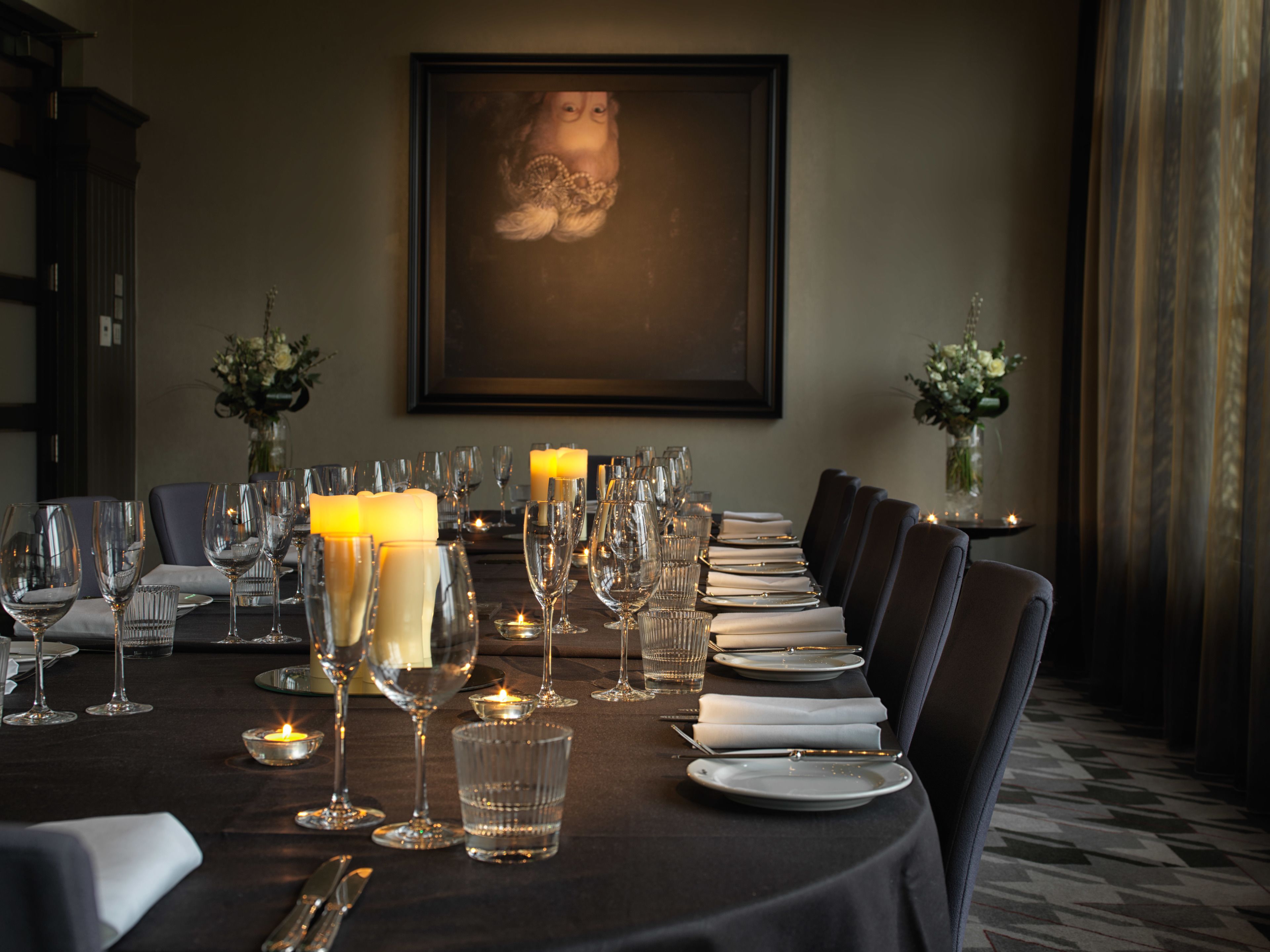 A formal dining table set with multiple wine glasses, plates, and candles, surrounded by chairs.