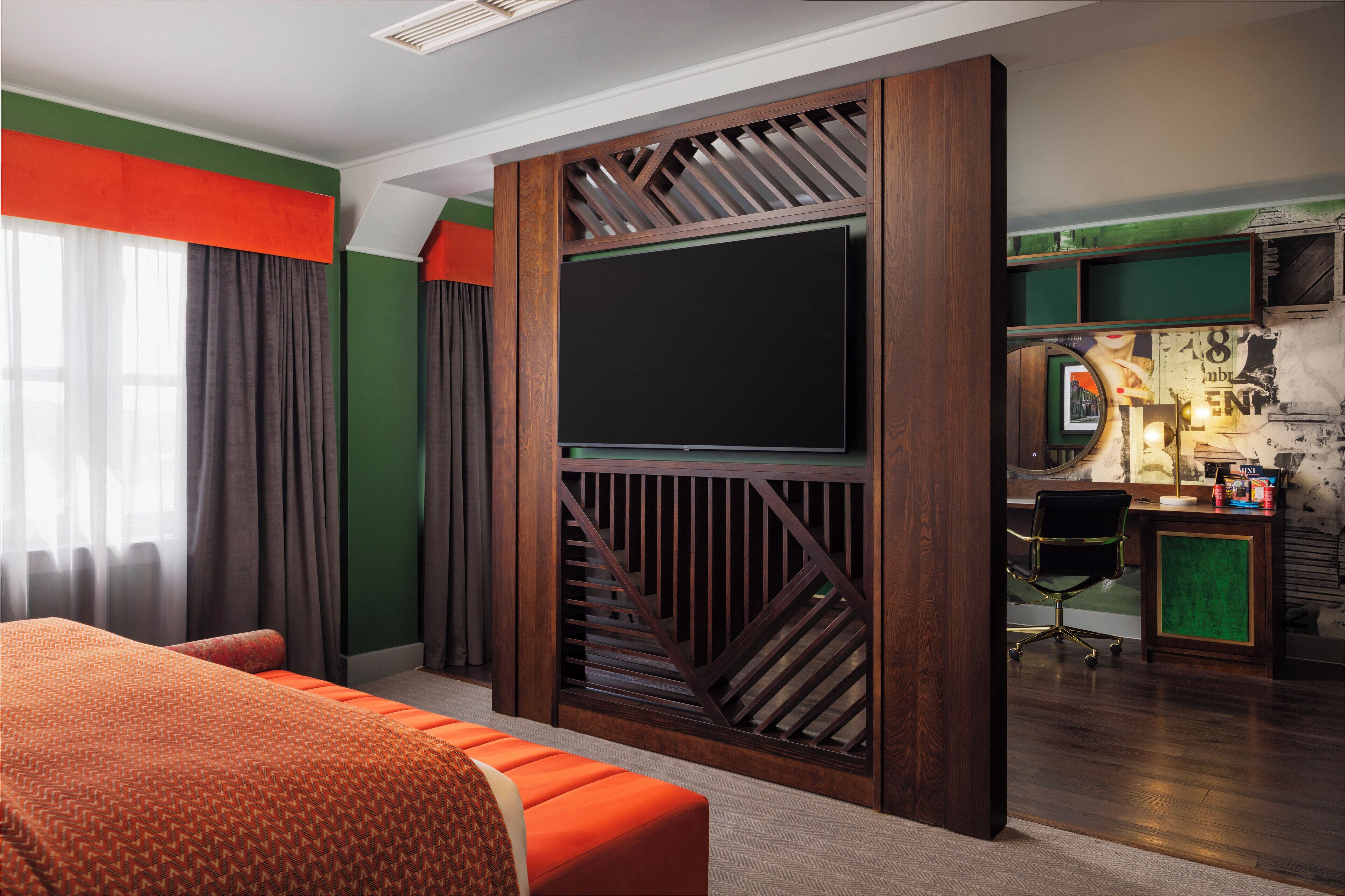 Ein Hotelzimmer mit einem großen Bett, einem an einer Holzvertäfelung montierten Fernseher, einem Schreibtisch mit Stuhl und einer grünen Akzentwand.