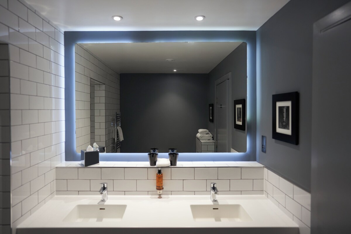 A modern bathroom with two sinks, a large mirror, and recessed lighting.