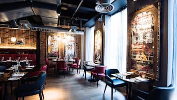 Interior de restaurante con paredes de ladrillo, suelo de madera y sillas tapizadas en rojo y azul.