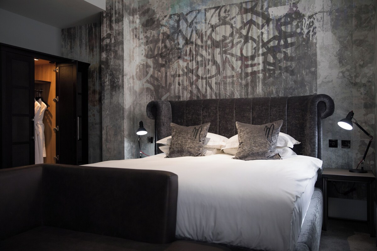 A modern bedroom with a large bed, dark headboard, and two bedside lamps.