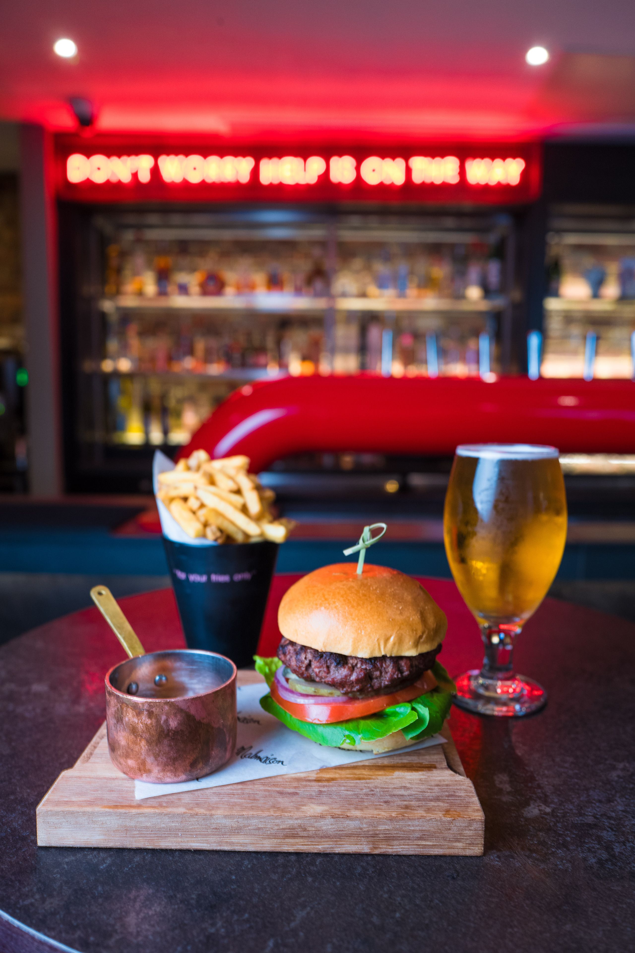 Una hamburguesa, papas fritas, una cerveza en un vaso y una taza sobre una tabla de madera.