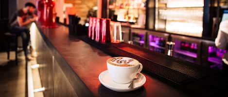 Una zona de bar con una taza de café sobre un platito, una barra y estantes con botellas.