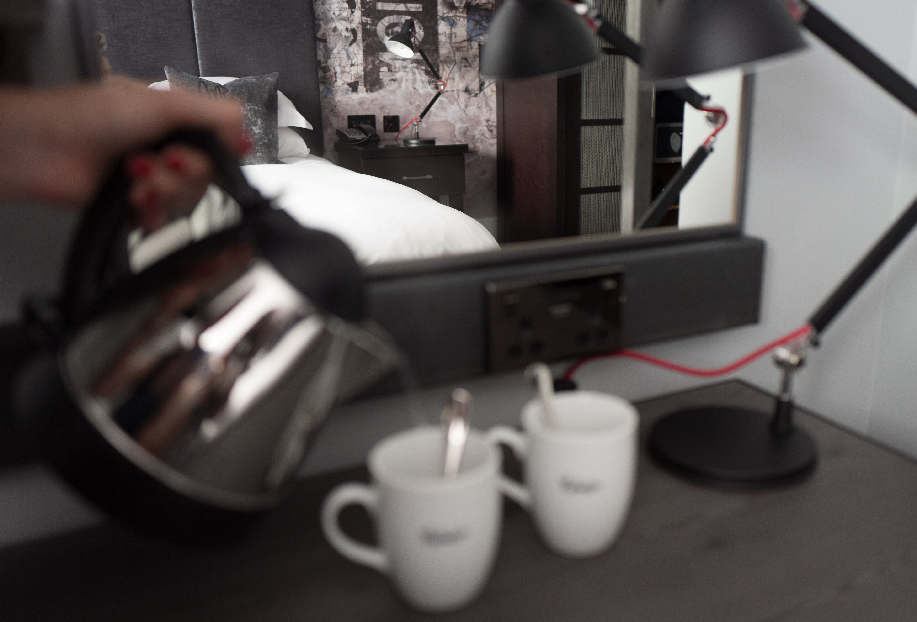 Una zona de cocina con un hervidor, dos tazas blancas y una lámpara negra sobre una mesa.