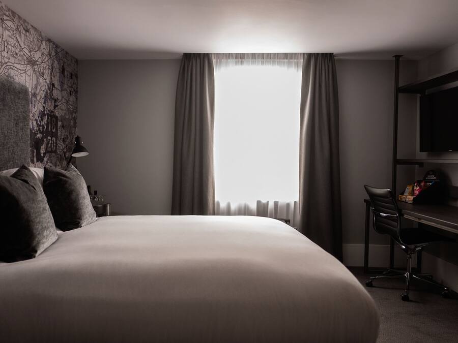 A modern hotel room with a large bed, a desk, and a TV mounted on the wall.