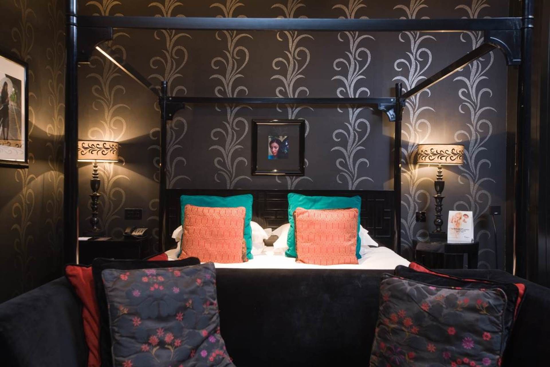A hotel room with a canopy bed, two pillows, a nightstand, and a framed picture on the wall.