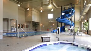 Una piscina interior con un jacuzzi, un tobogán azul y una zona de estar con sillas y mesas.