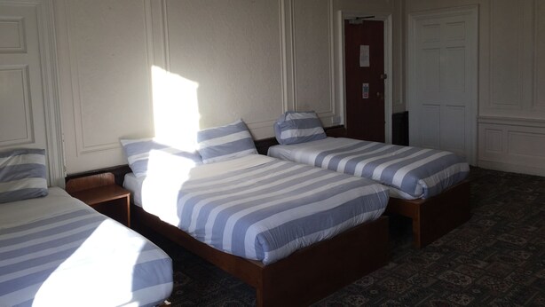 Quarto de hotel com três camas de solteiro, cada uma com roupa de cama listrada, cabeceira de madeira e mesa de cabeceira.