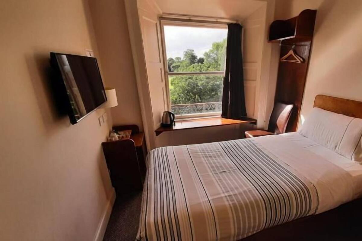 Une chambre d’hôtel avec un lit, une télévision, une fenêtre donnant sur un espace verdoyant, une chaise et une petite table.