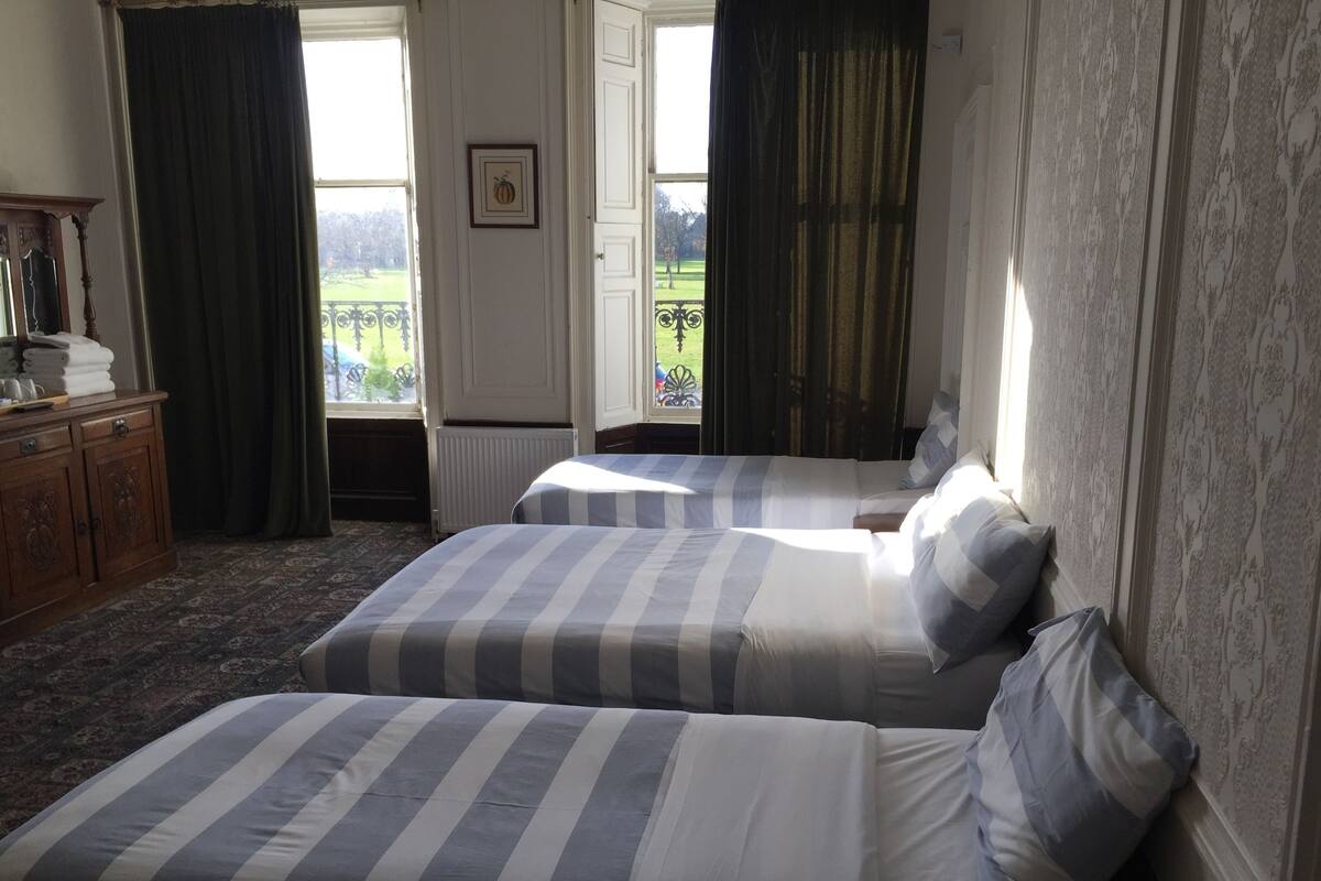 Une chambre d’hôtel avec deux lits, une commode, une fenêtre avec des rideaux et un radiateur.