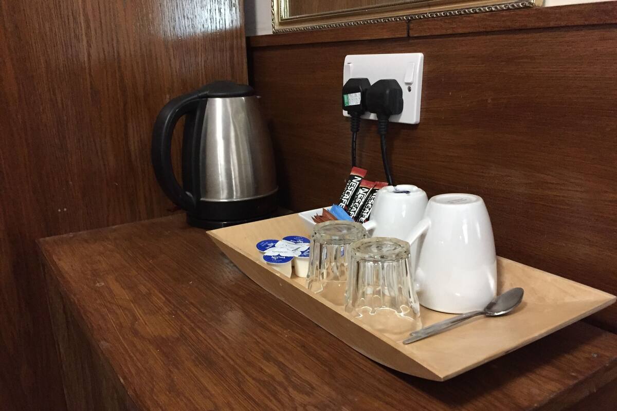 Une table en bois avec une machine à café, une bouilloire, une tasse blanche, une cuillère et quelques condiments.